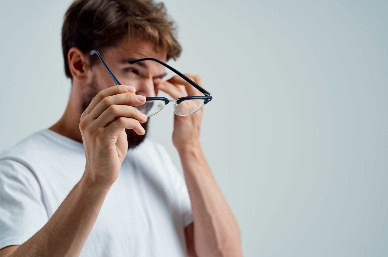 Homme blanc atteint de basse vision portant des lunettes, se frottant les yeux